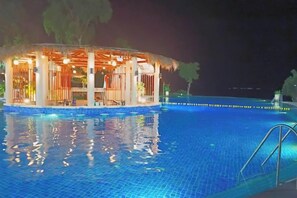 Een zwembad bij nacht met een overdekt gedeelte en een poolbar.