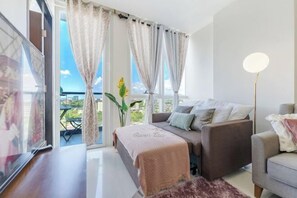 Una sala de estar moderna con sofá, mesa de centro, lámpara de pie y un amplio ventanal con cortinas.