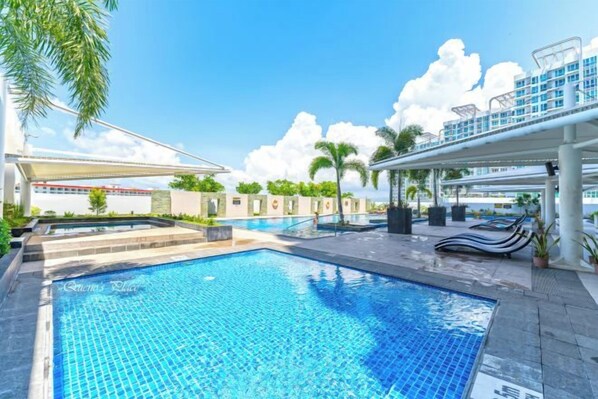 A swimming pool with lounge chairs and a covered area, surrounded by palm trees and a clear sky.
