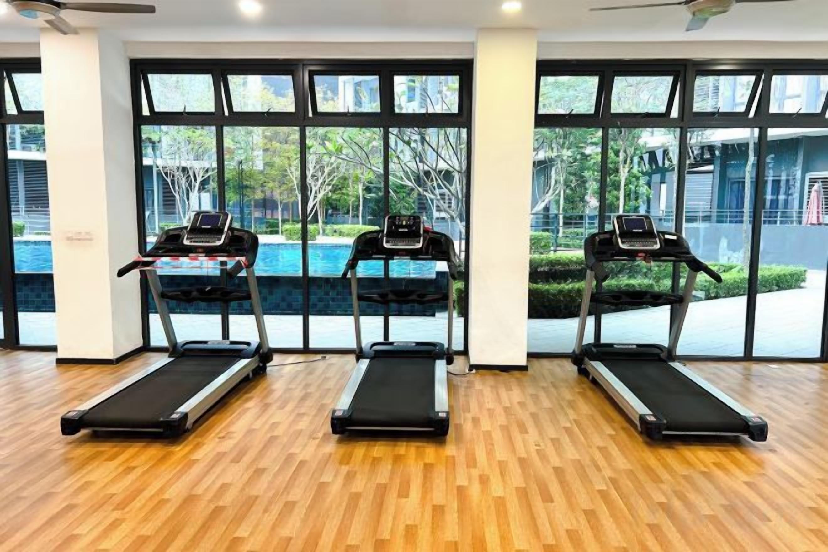 A gym with three treadmills, large windows, and a wooden floor.
