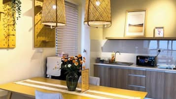 A modern kitchen with a dining table, pendant lights, and a vase of flowers.