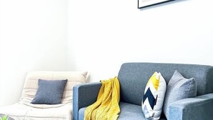En stue med sofa, stol og et gult pled.