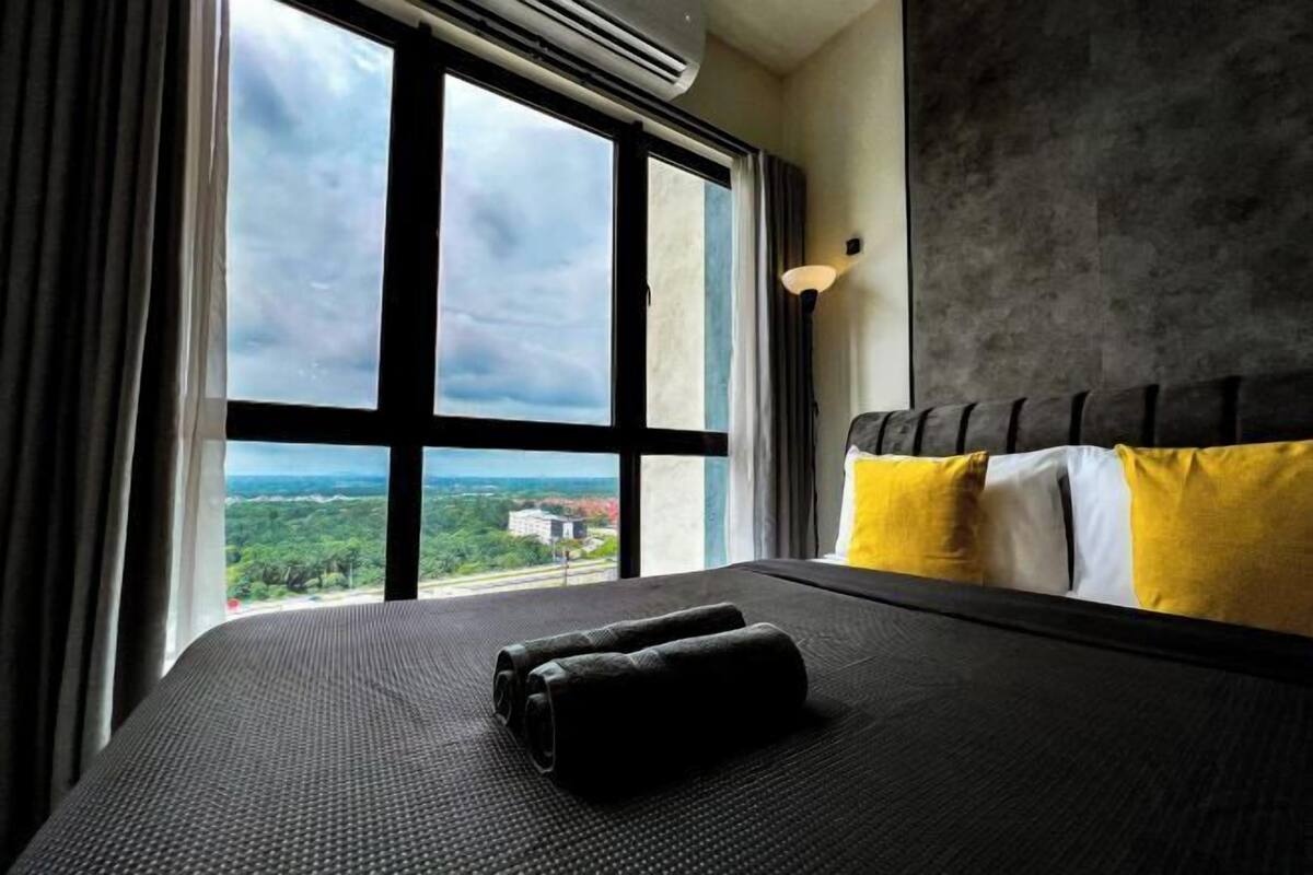 A hotel room with a large window, a bed with black and yellow bedding, and a grey headboard.