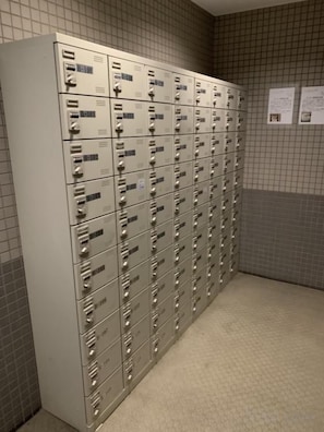 Una fila di armadietti metallici con etichette numeriche, un muro rivestito di piastrelle e un pavimento con moquette.