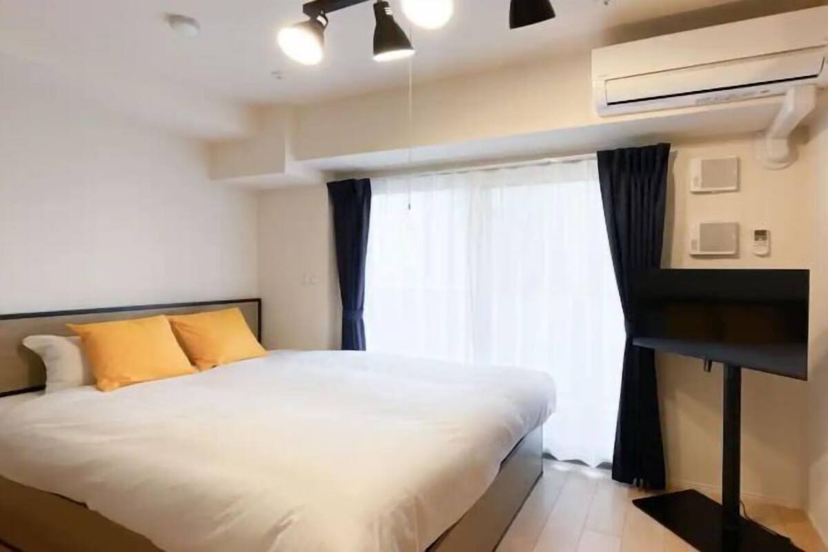 A hotel room with a bed, a TV, an air conditioning unit, and a window with curtains.