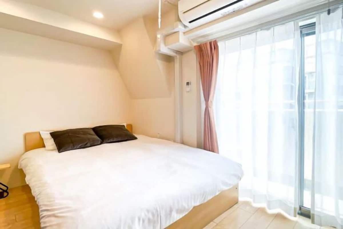 A bedroom with a bed, a window with sheer curtains, and an air conditioning unit.