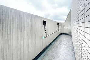 A corridor with a textured wall, a tiled floor, and two black handrails. - KISETSU Kagurazaka (Tokyo)