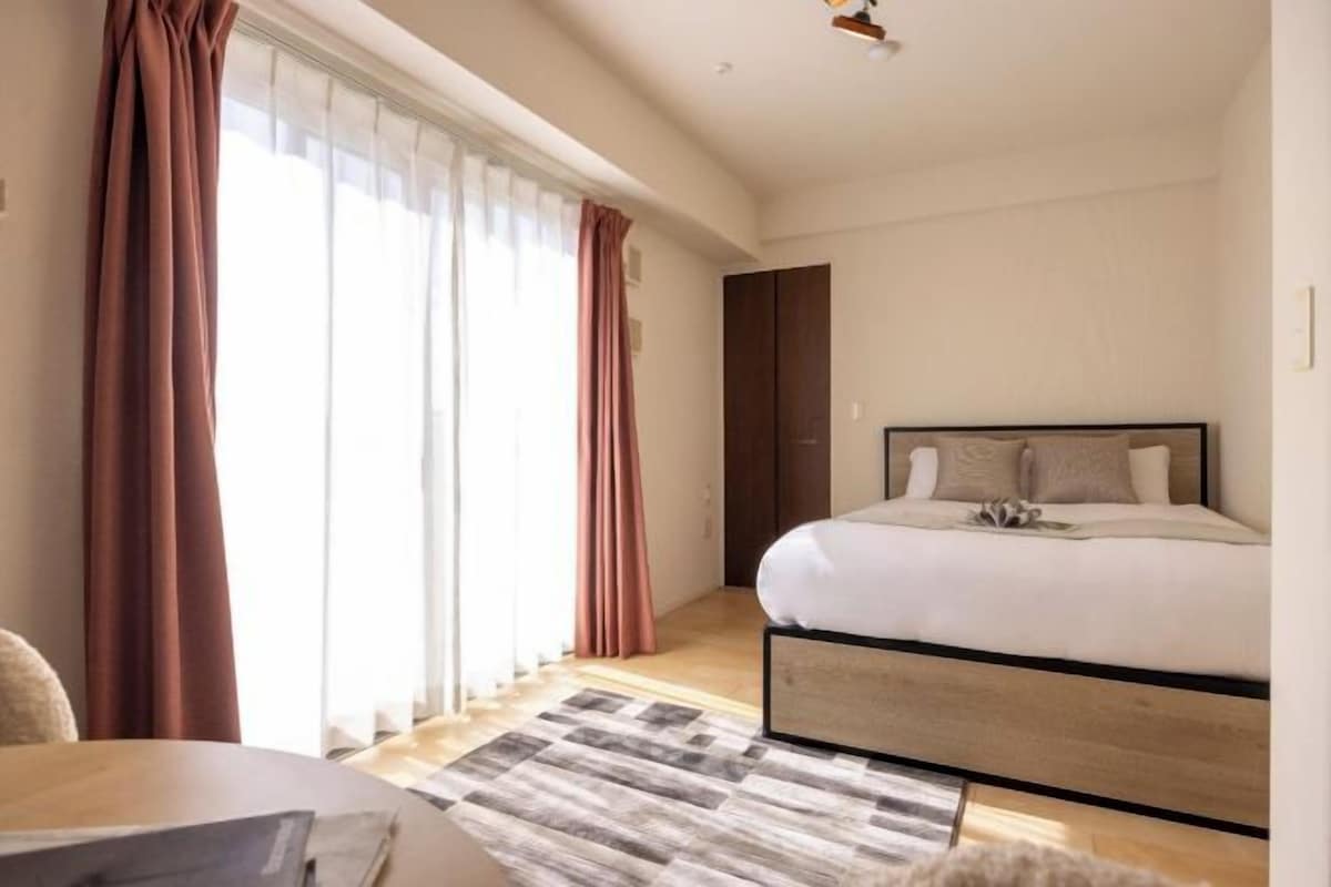A bedroom with a bed, a desk, and a window with curtains.