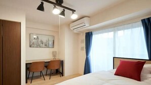 Ein Hotelzimmer mit einem Bett, einem Schreibtisch mit zwei Stühlen, einer Klimaanlage und einem Fenster mit Vorhängen.