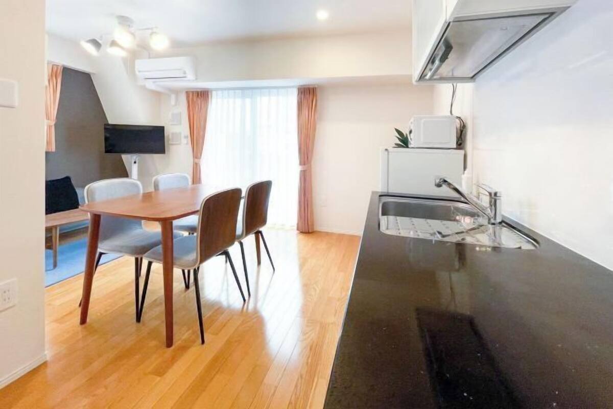 A compact kitchen with a black countertop, a built-in oven, and a sink. There is a dining area with a wooden table and four chairs.