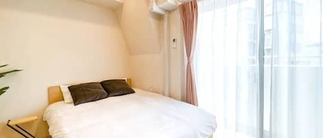 A bedroom with a bed, a window with curtains, and an air conditioning unit.