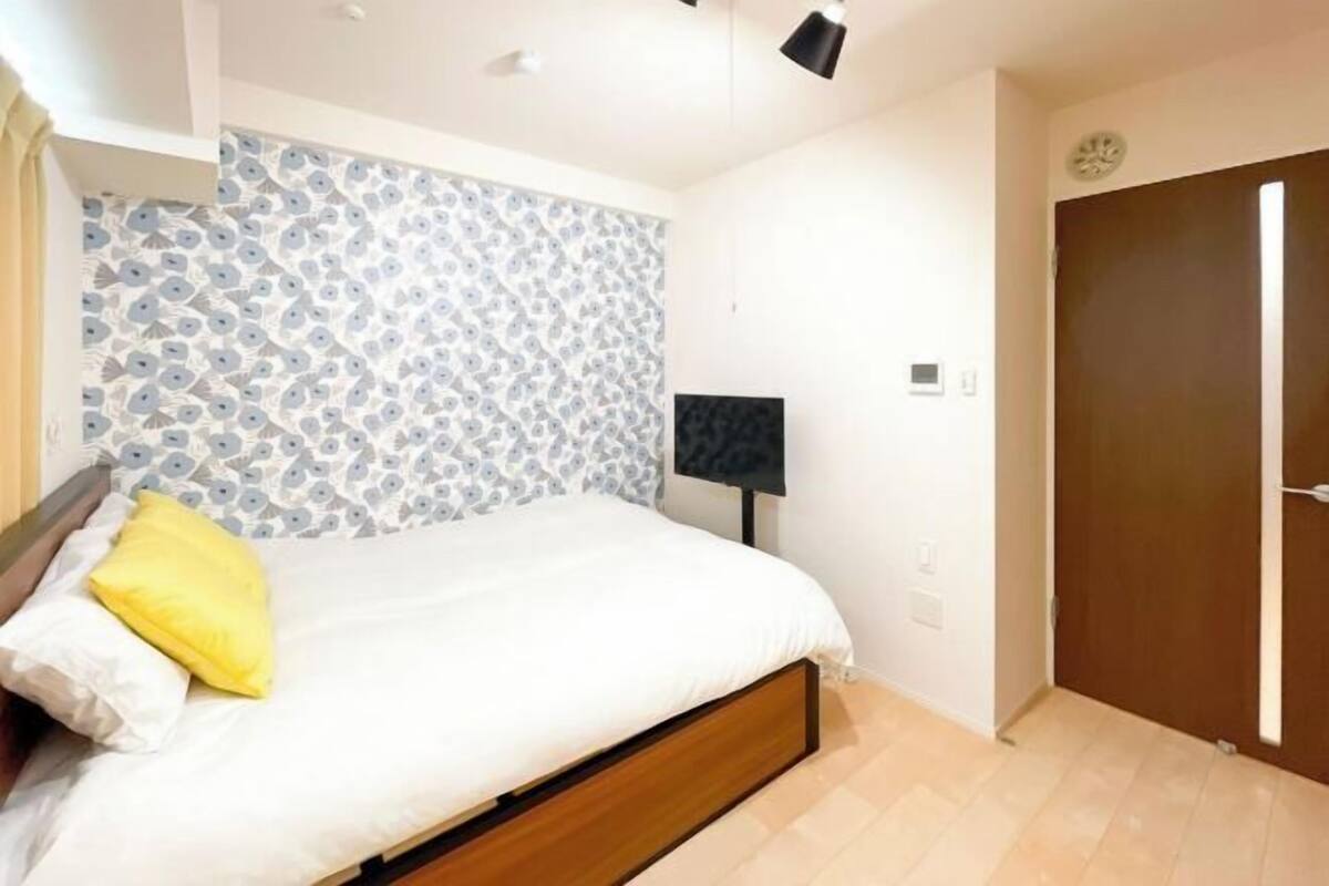A bedroom with a bed, a patterned wall, a door, and a nightstand with a lamp.