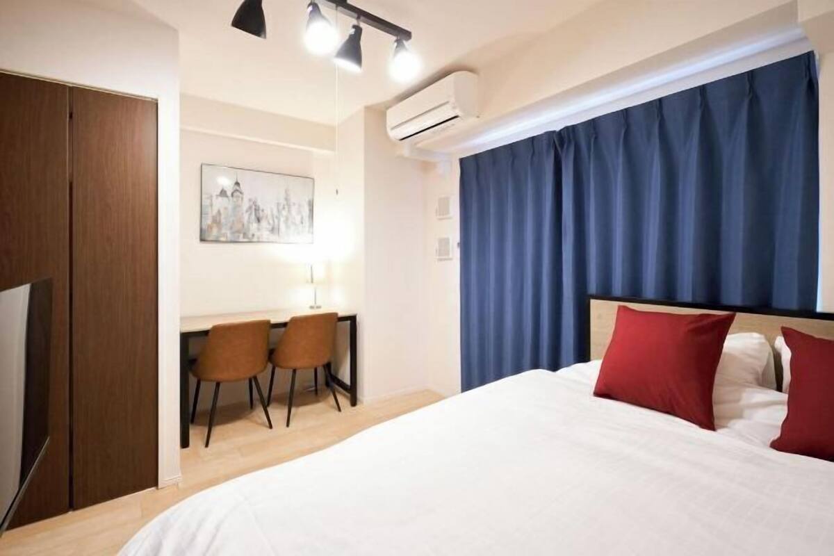 A hotel room with a bed, a desk with two chairs, a wardrobe, and an air conditioning unit.