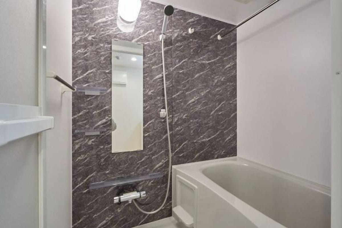 A bathroom with a marble wall, a bathtub, a shower, and a mirror.