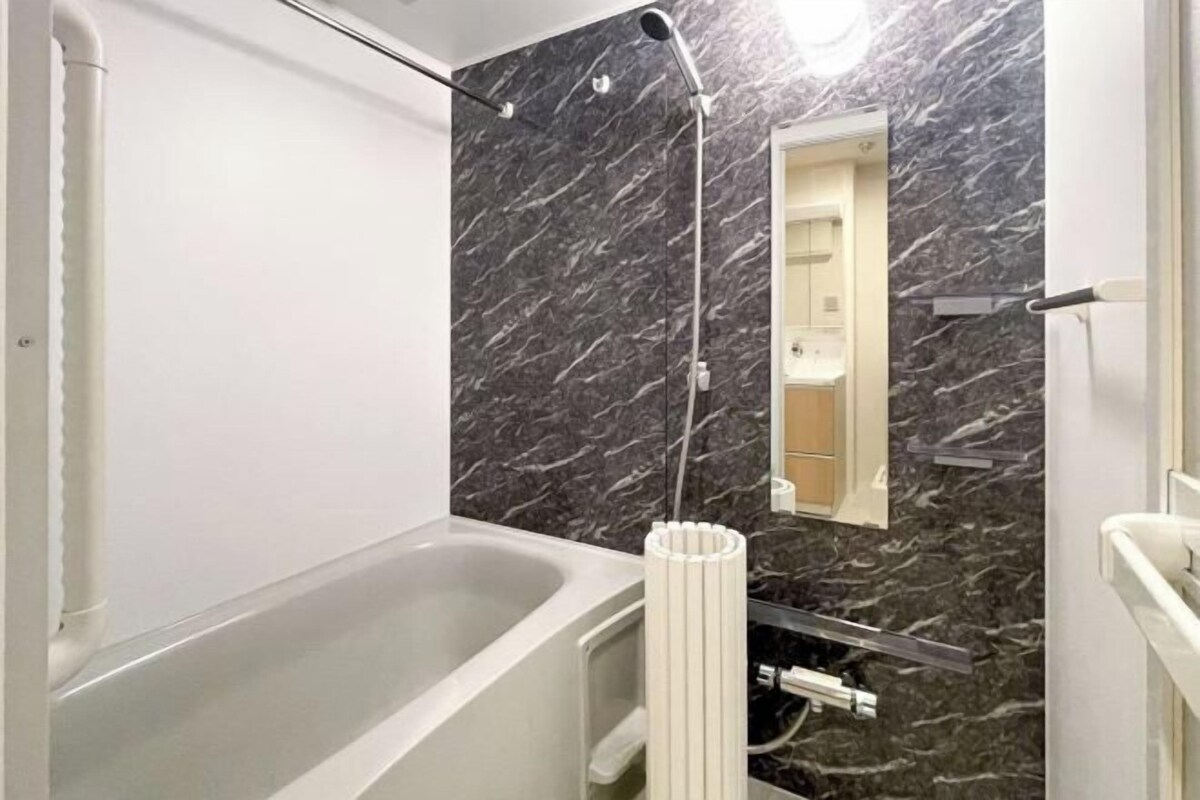 A modern bathroom with a marble wall, a bathtub, a shower, and a toilet.