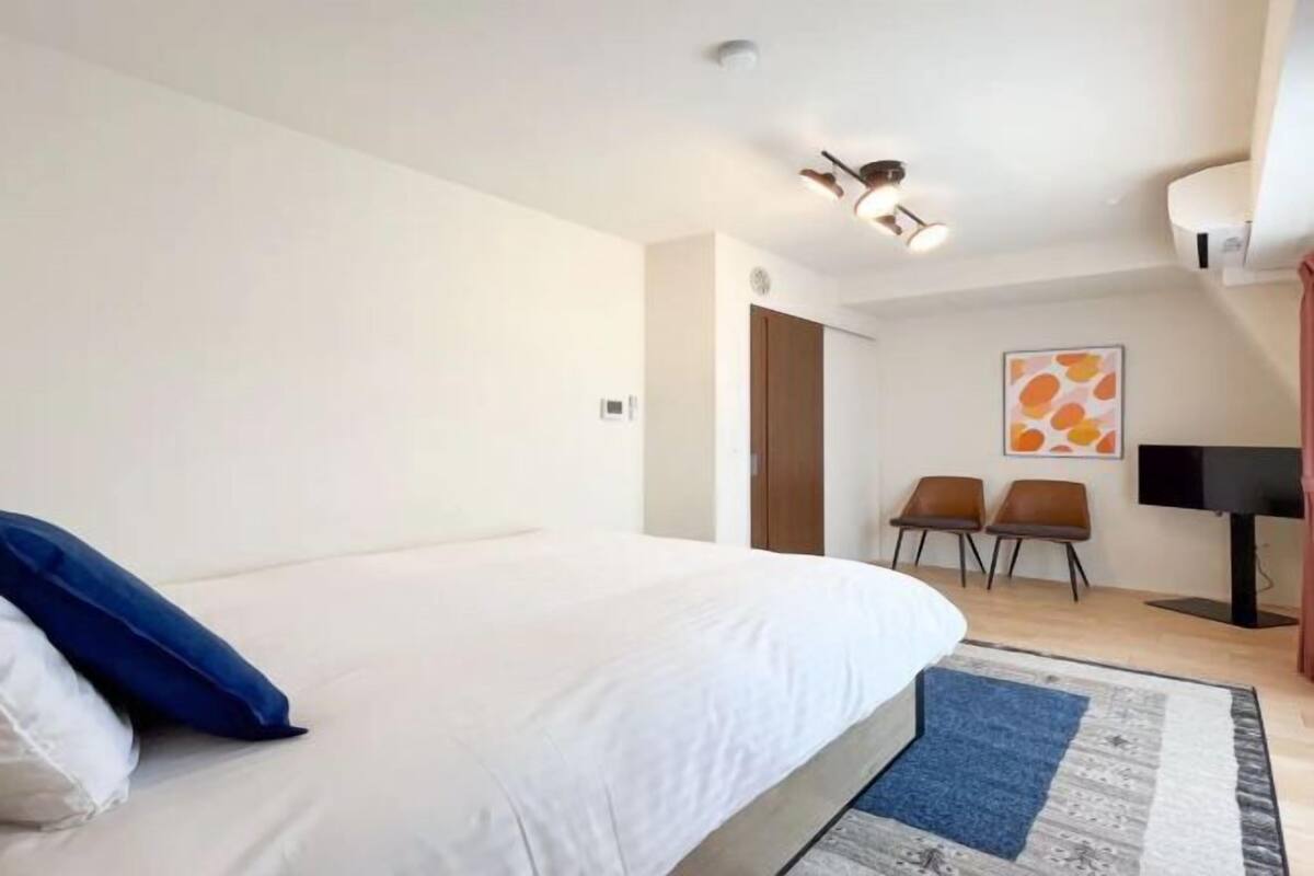 A bedroom with a bed, a desk, two chairs, a TV, and a ceiling light fixture.
