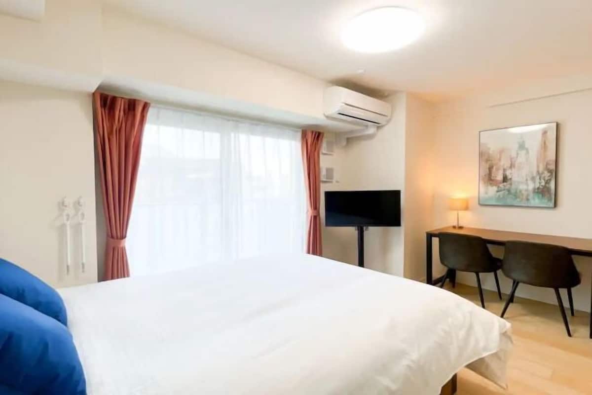 A hotel room with a bed, a desk, two chairs, an air conditioning unit, and a painting on the wall.