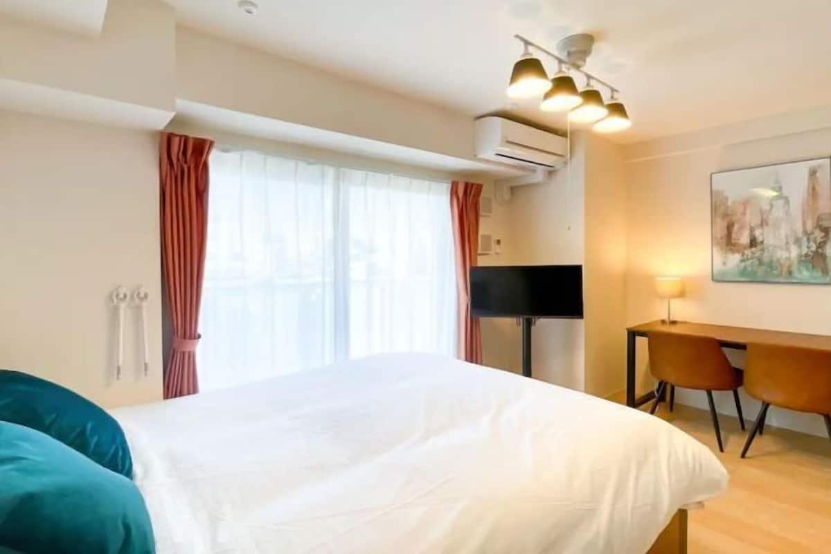 A hotel room with a bed, a desk, two chairs, a TV, and a painting on the wall.