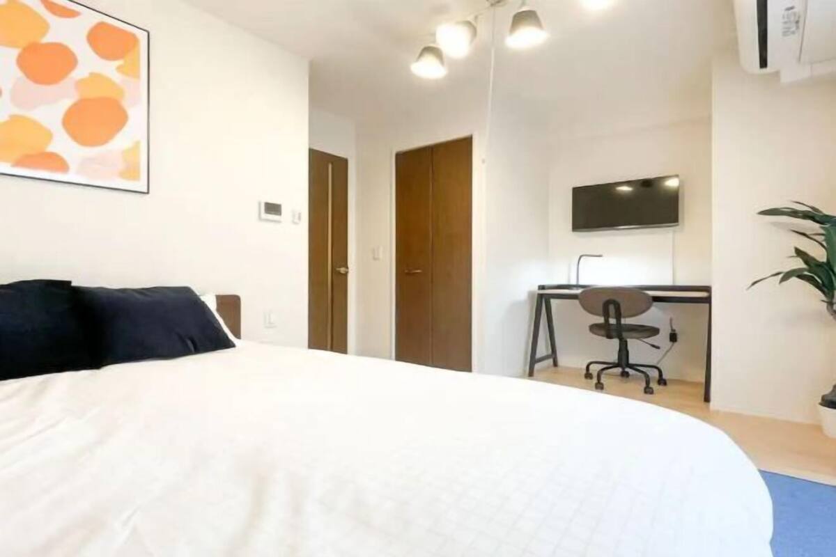 A hotel room with a bed, a desk, a chair, a TV, and a potted plant.