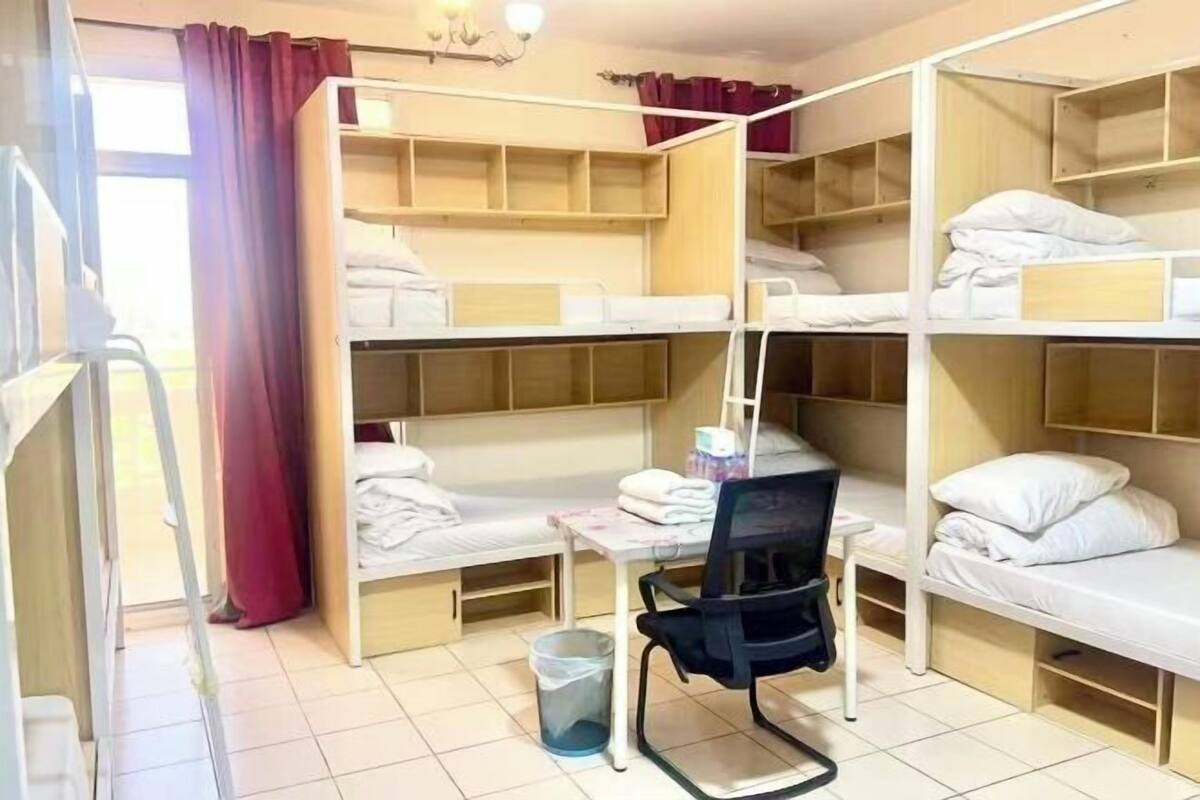 Une chambre de dortoir avec des lits superposés, un bureau, une chaise et une poubelle.