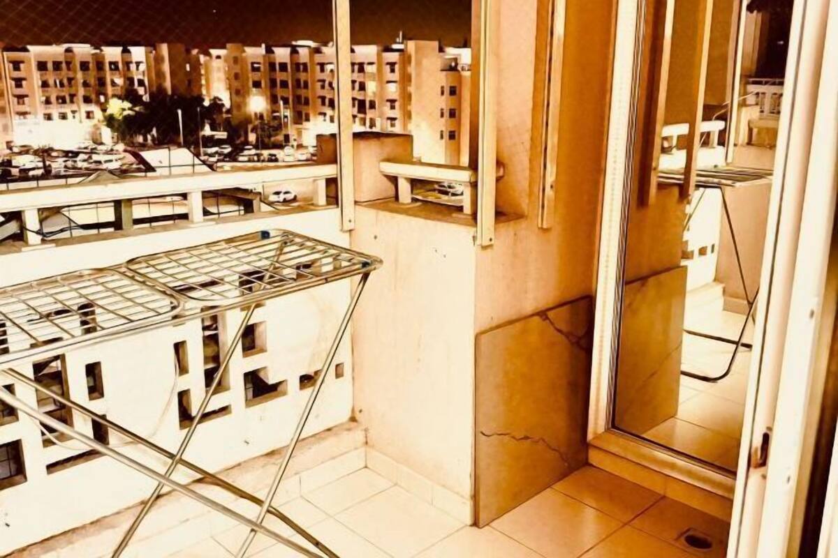 Un balcon doté d’un étendoir métallique, une porte vitrée donnant sur une salle de bain et une vue sur un quartier résidentiel avec ses immeubles.