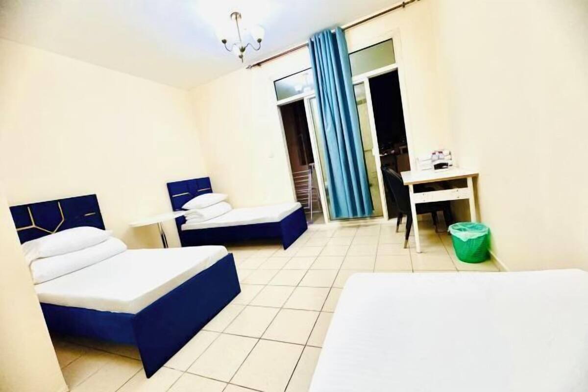 Une chambre d’hôtel avec deux lits, un bureau, une chaise, une poubelle et une porte coulissante.