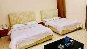 Habitación de hotel con dos camas, una mesita pequeña con una botella de agua y una mesita de noche con una lámpara.