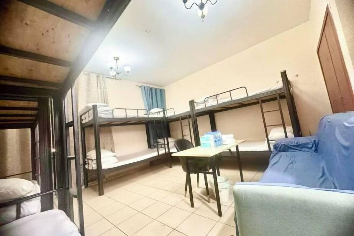 Une chambre de dortoir avec des lits superposés, une table avec des chaises, un bureau et un luminaire au plafond.