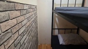 A small, narrow room with a brick-patterned wall and a bunk bed with a black frame. - Orange Home Vacation (Dubai)