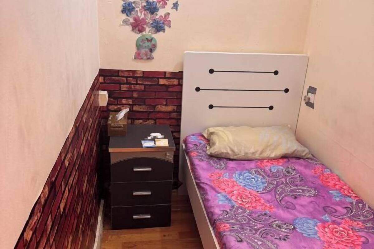A small bedroom with a bed, a dresser with drawers, a brick accent wall, and a floral wall decoration.