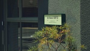 A sign for Hotel ORTO with a modern building facade and a window in the background. - At Hotel ORTO (Fukuoka)