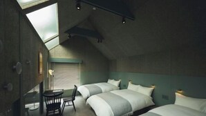 A compact room with two beds, a small table, and a chair. There is a skylight above the beds, and the walls are painted in a muted green color. - At Hotel ORTO (Fukuoka)