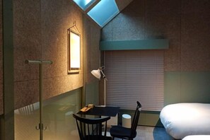 A room with a glass partition, a table with chairs, a lamp, and a bed. - At Hotel ORTO (Fukuoka)