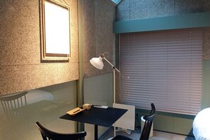 A small room with a table, a chair, a desk lamp, and a window with blinds. - At Hotel ORTO (Fukuoka)