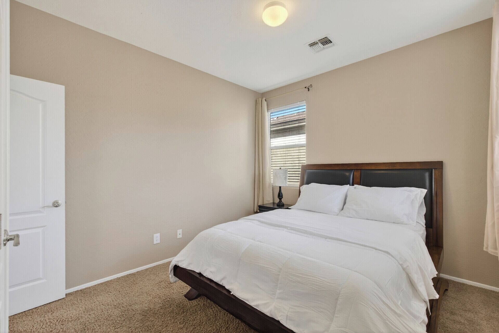 A bedroom with a bed, a nightstand, a window with blinds, and a door.