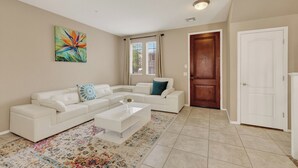 A living room with a white sectional sofa, a coffee table, a colorful rug, a door, and a painting on the wall.
