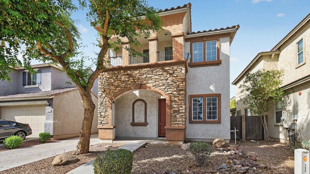 A two-story house with a stone archway entrance, a garage, and a well-maintained front yard with rocks and shrubs.