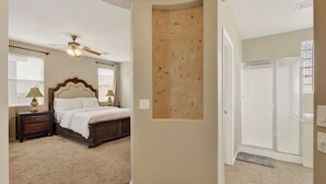 A bedroom with a bed, nightstands, a ceiling fan, a window with blinds, and a door leading to a bathroom.