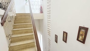 A staircase with a wooden handrail and beige steps, leading to a landing with a white wall and two framed pictures. - Hoe Stay - Where to stay (Hanoi)