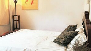 A bedroom with a bed, patterned pillows, a floor lamp, and a wall art piece. - Hoe Stay - Where to stay (Hanoi)