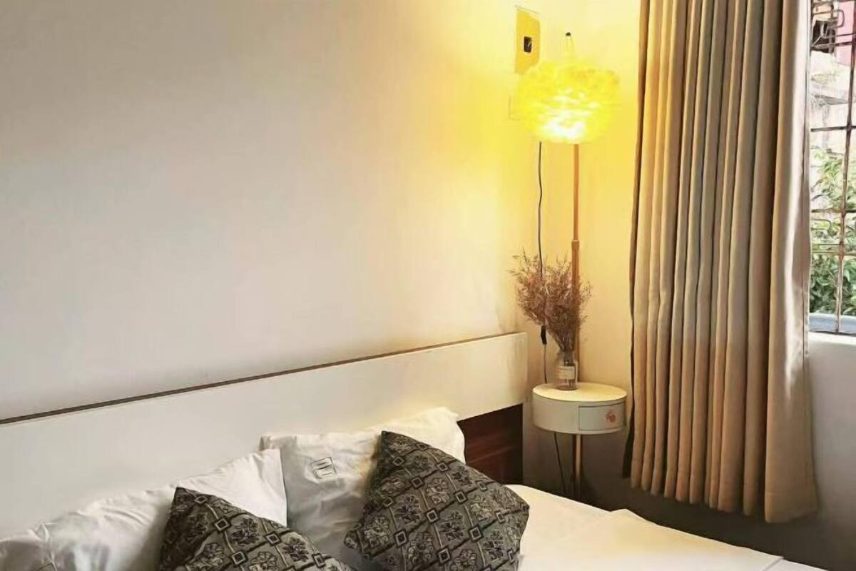 Une chambre d’hôtel avec un lit, des oreillers, une table de chevet avec une lampe et une fenêtre avec des rideaux.