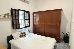 A bedroom with a bed, a wardrobe, a window with blinds, and a potted plant.