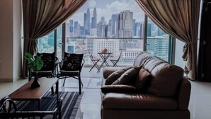 Una sala moderna con un sofá de cuero, dos sillones, una mesita y vistas a un horizonte urbano a través de grandes ventanales.