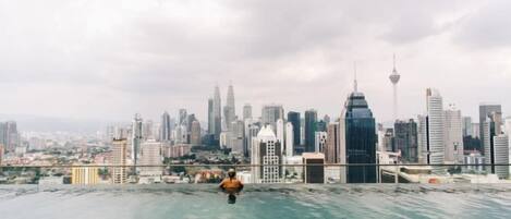 Une vue sur les gratte-ciel d’une ville, avec une personne debout au bord d’une piscine sur un toit.
