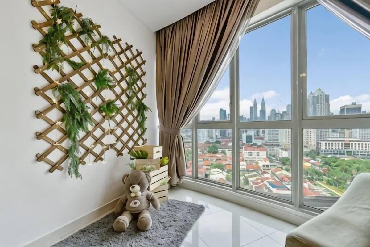 Una habitación con un ventanal grande, un osito de peluche, un muro de celosía de madera y vistas de un paisaje urbano.