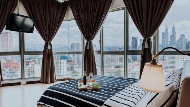 Habitación de hotel con una cama grande, televisión, lámpara y vista a un paisaje urbano.