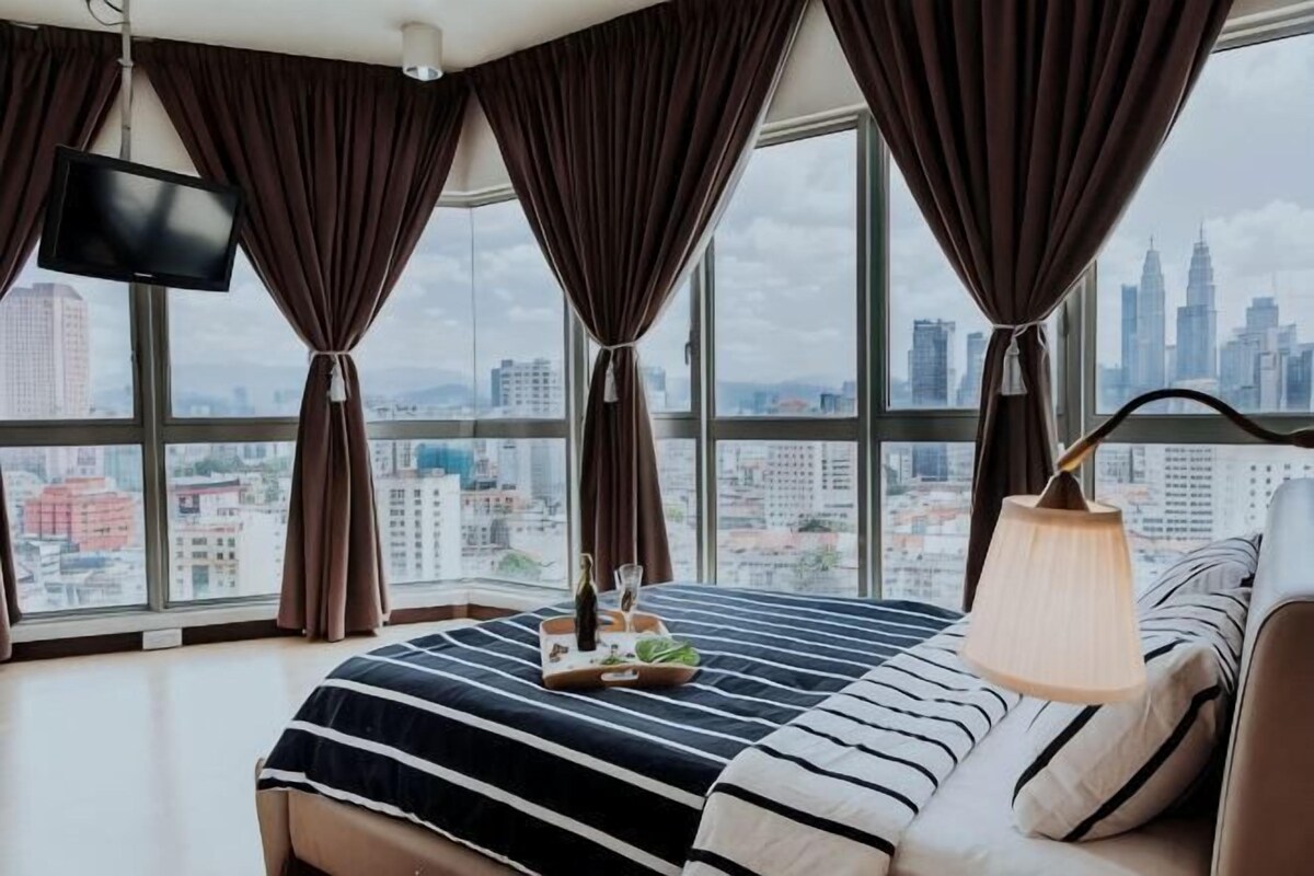 A hotel room with a large bed, a TV, a lamp, and a view of a cityscape.
