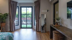 A room with a sliding glass door to a patio, a bed with a green leaf pattern, a wooden floor, a TV on a stand, and a wall-mounted air conditioner.
