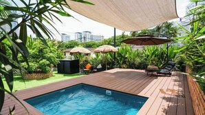 A swimming pool with a wooden deck, surrounded by umbrellas and lounge chairs.
