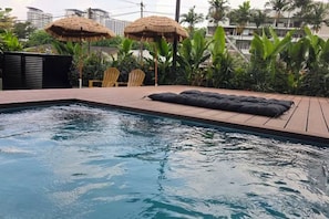 A swimming pool with a wooden deck, lounge chairs, and thatched umbrellas.